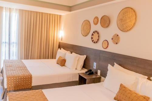 Quarto de hotel com duas camas de casal, decoração em tons de bege aconchegantes, obras de arte em tecido na parede e cortinas do chão ao teto.