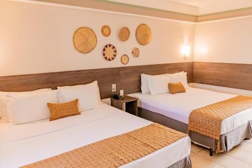 Quarto de hotel luminoso com duas camas, decoração de parede em vime e detalhes em madeira aconchegantes.