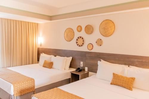 Quarto de hotel com duas camas, decoração em tons de bege aconchegante, obras de arte na parede e um abajur.