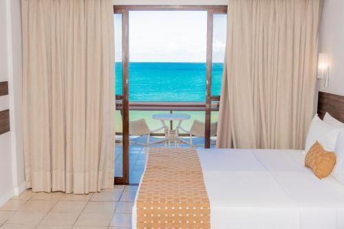 Quarto de hotel com cama de frente para portas de correr que dão para uma varanda com vista para o mar azul-turquesa.