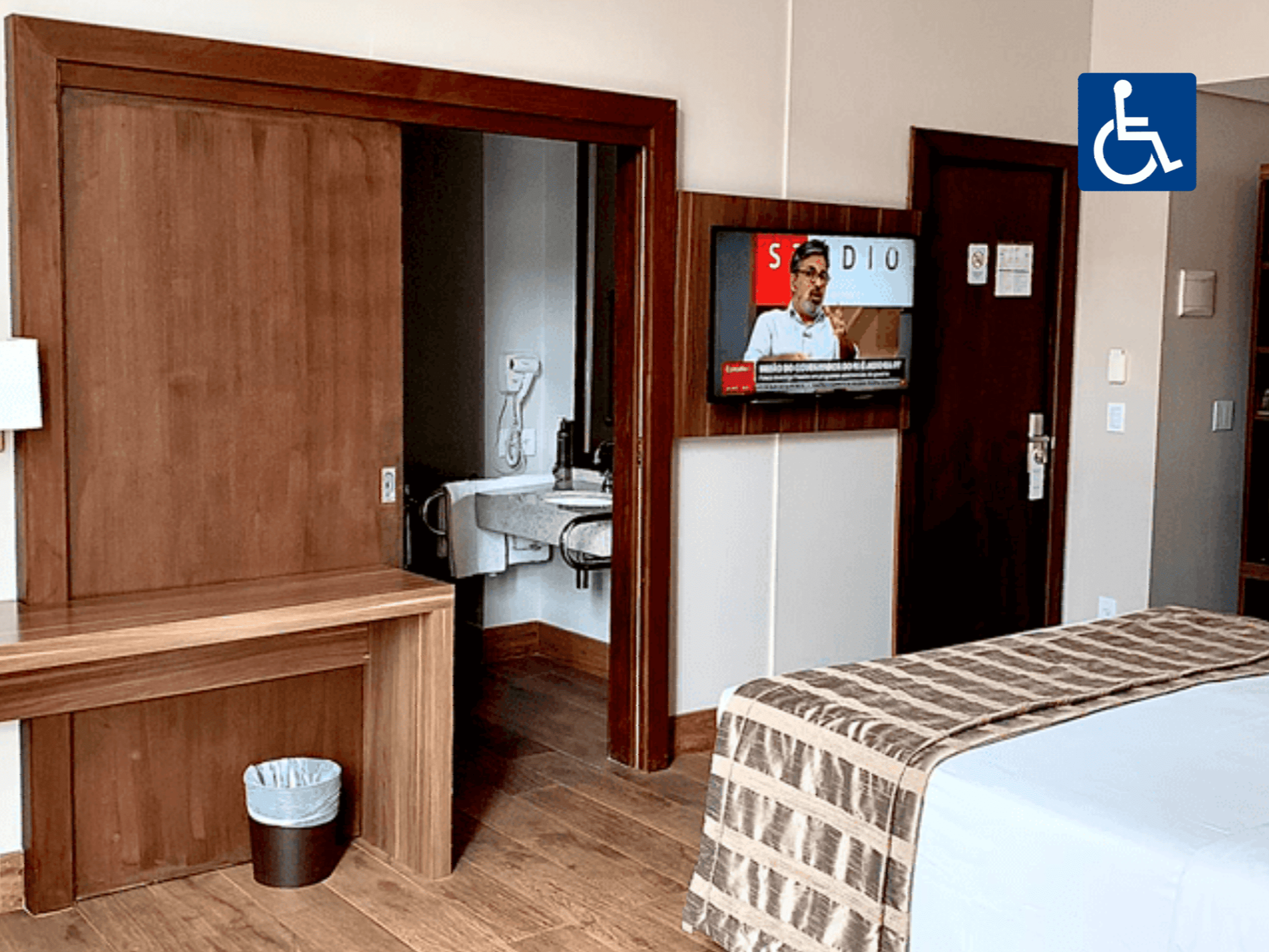 Quarto de hotel acessível com cama, escrivaninha e porta de banheiro aberta.