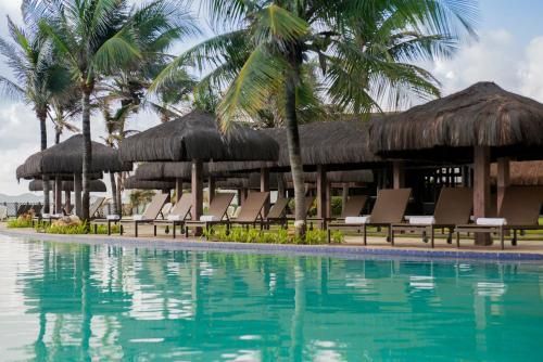 Piscina do resort com palmeiras, cabanas de palha e espreguiçadeiras à beira da água turquesa.
