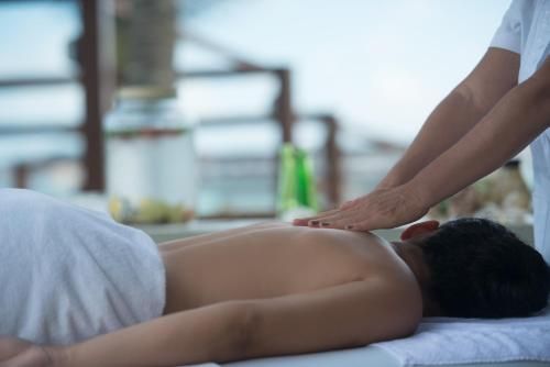 Pessoa recebendo uma massagem nas costas em uma maca de spa ao ar livre, enquanto outra mão aplica pressão.