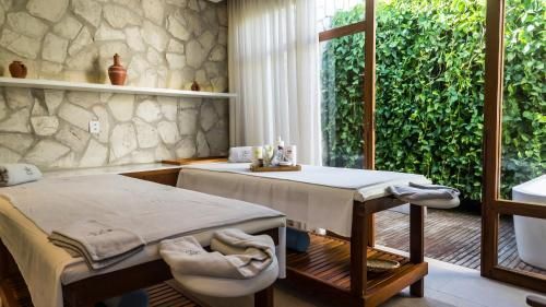 Mesa de massagem em uma sala de spa serena com parede de pedra, banco de madeira e grande janela com vista para a folhagem verde.