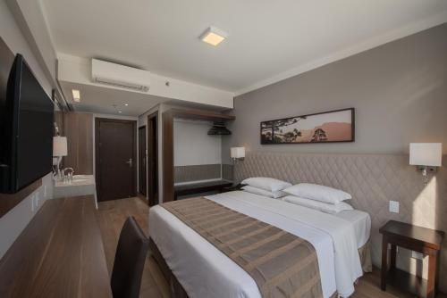 Quarto de hotel moderno com duas camas de solteiro, TV de parede, escrivaninha e decoração bege.
