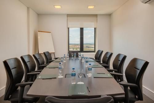 Sala de conferências com uma mesa comprida, cadeiras pretas, um quadro branco e vista para a janela.