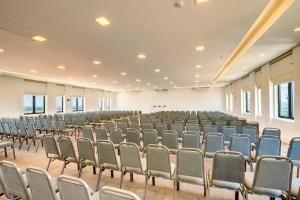 Sala de conferências vazia com fileiras de cadeiras cinzentas e luzes brilhantes no teto.