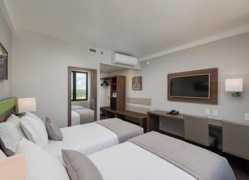 Quarto de hotel moderno com duas camas de solteiro, TV de parede, escrivaninha, espelho e decoração em tons neutros de cinza.