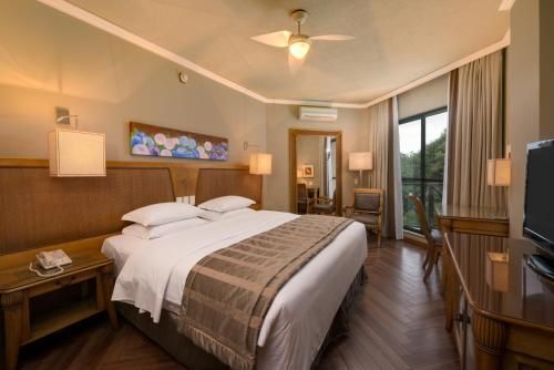 Quarto de hotel moderno com cama king-size, móveis de madeira, luminárias e varanda com vista.