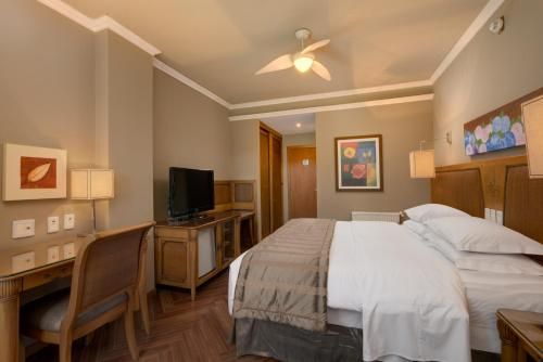 Quarto de hotel aconchegante com cama king-size, escrivaninha, TV e decoração em tons de bege quente.