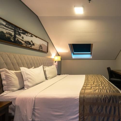 Quarto de hotel moderno com cama grande, teto inclinado, obras de arte na parede e uma pequena janela de teto.