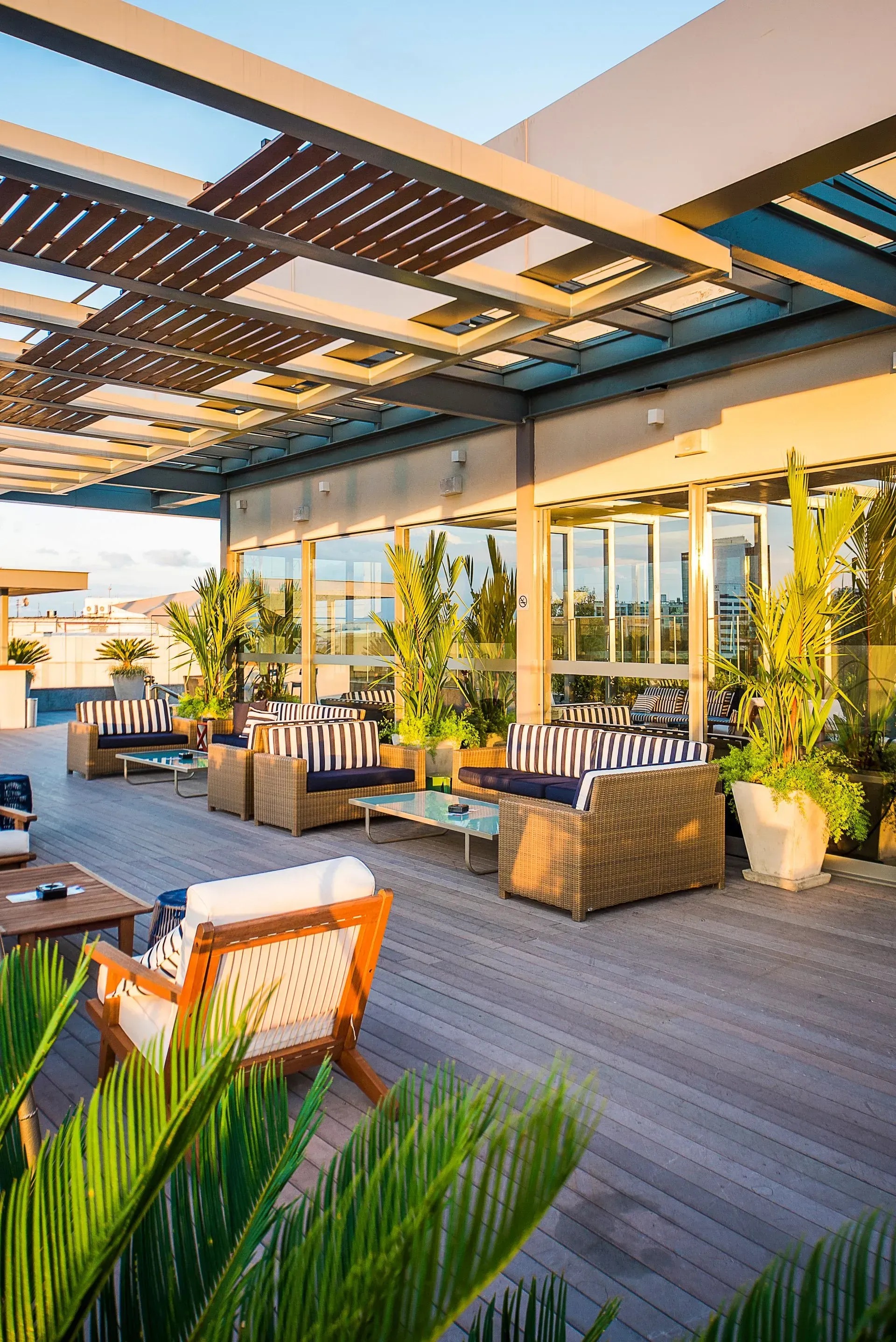 Terraço moderno na cobertura com cadeiras de vime, plantas em vasos e uma pérgola, banhado por um sol aconchegante.