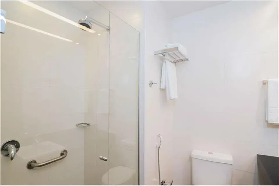 Banheiro minimalista branco com box de vidro, porta-toalhas, vaso sanitário e pia suspensa.