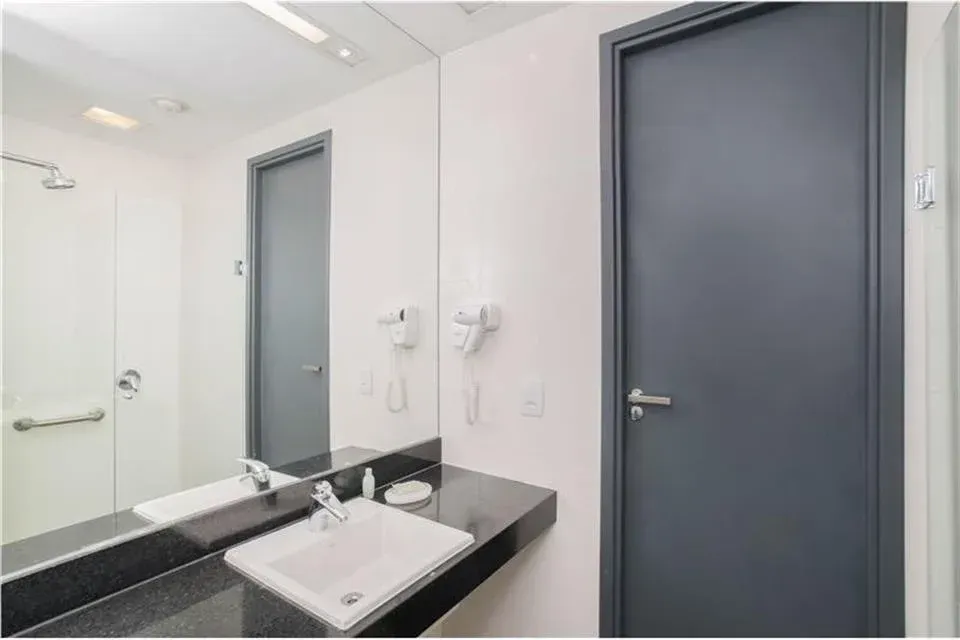 Banheiro moderno com portas cinza, espelho grande e bancada preta com pia branca e acessórios de parede.