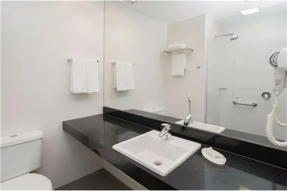 Banheiro moderno branco com bancada, pia, espelho e box de vidro pretos.