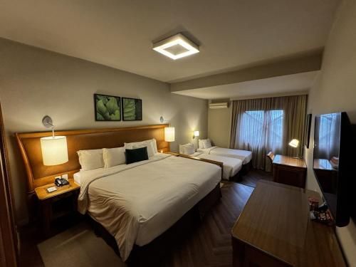 Quarto de hotel com duas camas, luminárias aconchegantes, janela e obras de arte na parede.