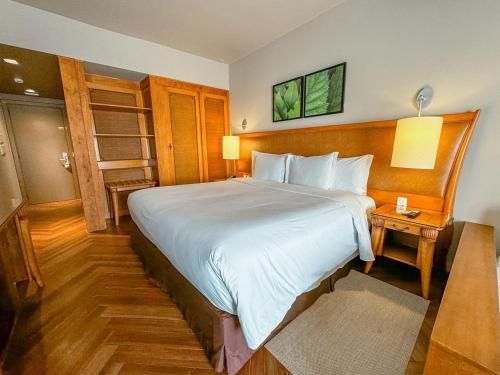 Quarto de hotel luminoso com uma cama grande, móveis de madeira e abajures aconchegantes.