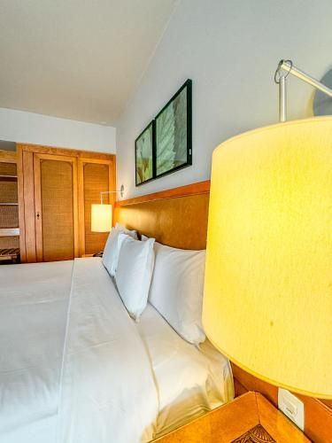 Quarto de hotel luminoso com cama king-size, lençóis brancos, cabeceira de madeira e abajures com luz aconchegante.