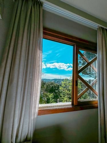 Janela aberta com moldura de madeira, cortinas brancas e vista para o céu azul e as montanhas lá fora.