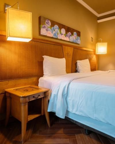Quarto de hotel aconchegante com cama bem arrumada, mesa de cabeceira de madeira e obra de arte na parede acima da cabeceira.