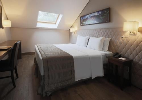 Quarto aconchegante com claraboia, cama king-size, abajures e escrivaninha junto à janela.