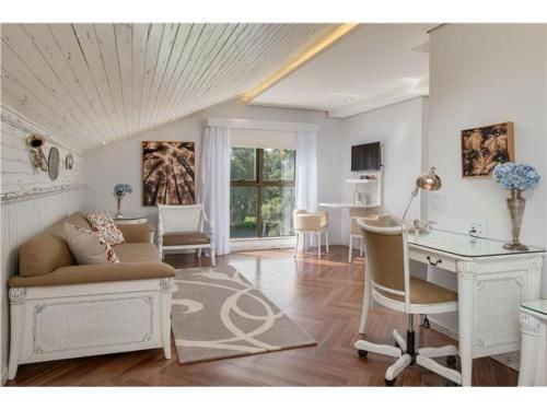Sala de estar iluminada com escrivaninha branca, sofá, tapete, portas de vidro deslizantes e decoração em tons neutros suaves.