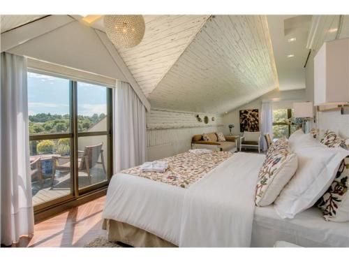 Quarto luminoso no sótão com teto abobadado branco, cama king-size e portas de varanda com vista panorâmica.