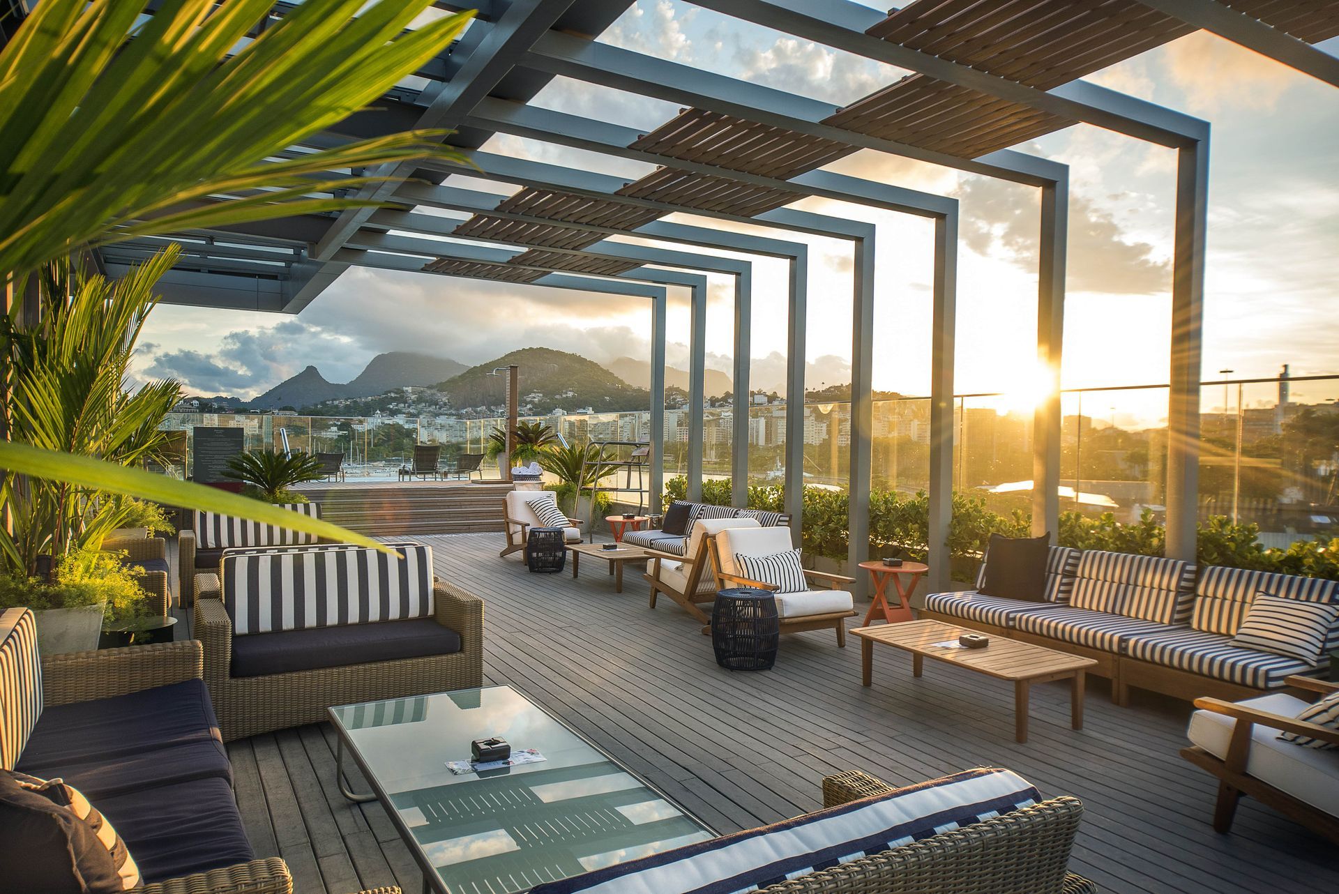 Terraço na cobertura com vista para o pôr do sol, espreguiçadeiras, pérgola e para as montanhas sobre a água.