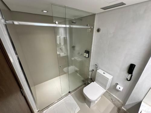 Banheiro moderno com box de vidro, vaso sanitário branco e telefone preto fixado na parede.