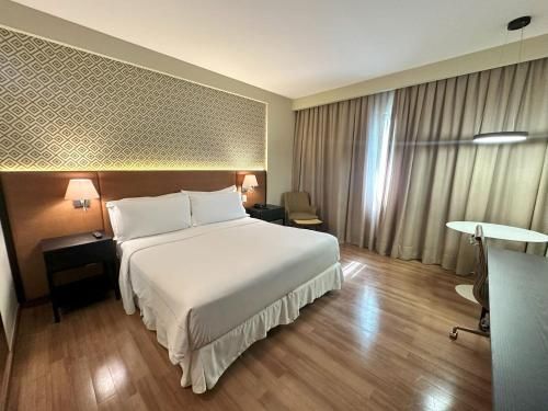 Quarto de hotel moderno com cama, piso de madeira, parede estampada, cortinas, escrivaninha e cadeira.