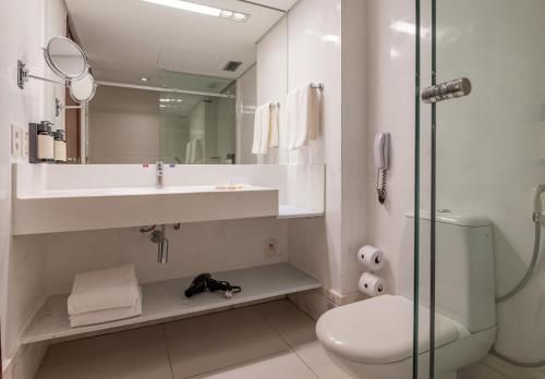 Banheiro moderno branco com pia, espelho, box de vidro, porta-toalhas e vaso sanitário próximo ao box.