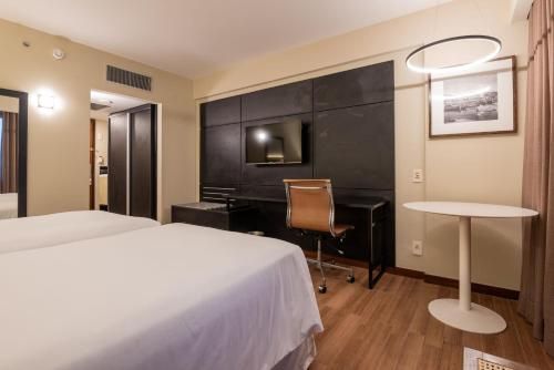Quarto de hotel com duas camas, escrivaninha, TV de parede e mesa redonda pequena.