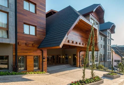 Exterior de hotel moderno em estilo rústico, com revestimento de madeira, telhados inclinados e um pátio de entrada pavimentado.