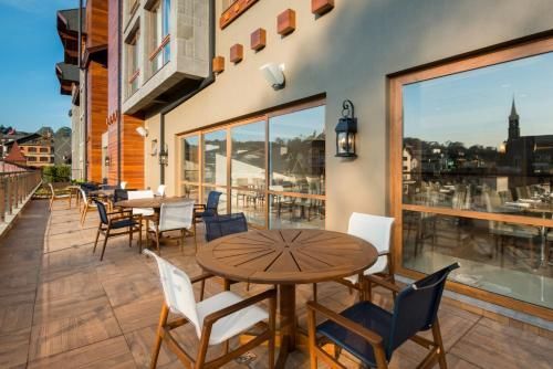 Terraço na cobertura com mesas e cadeiras de madeira ao lado de grandes janelas com vista para o horizonte da cidade.