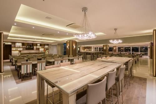 Sala de jantar elegante de restaurante com mesas compridas, cadeiras estofadas e um lustre sob iluminação aconchegante.