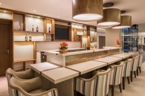 Interior de restaurante moderno com um longo balcão de mármore, banquetas bege e prateleiras de madeira em tons quentes.