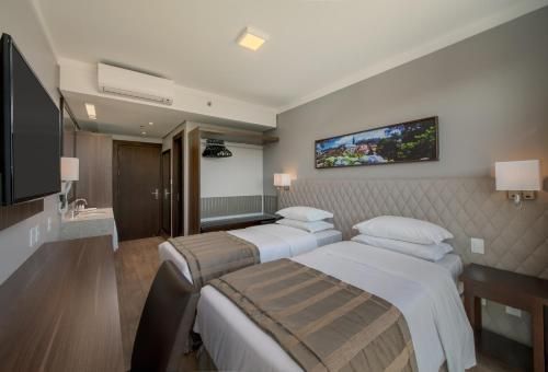 Quarto de hotel moderno com duas camas de solteiro, paredes cinza, TV e um pequeno abajur.