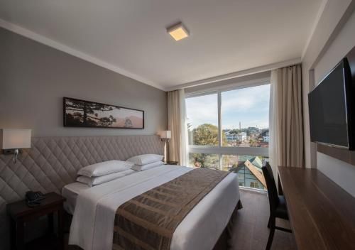 Quarto de hotel moderno com cama, obras de arte na parede, TV e janela ampla com vista para a cidade.