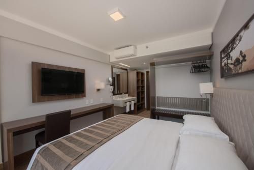 Quarto de hotel moderno com cama, escrivaninha, TV de parede e espelho grande.