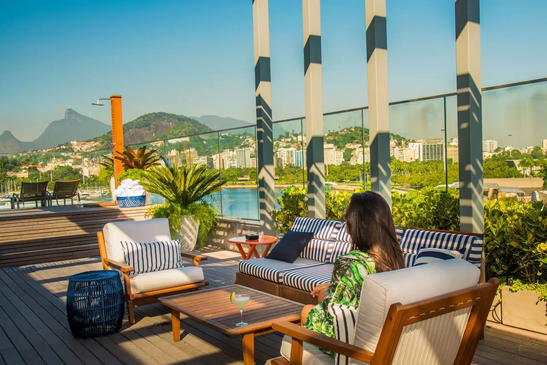 Lounge na cobertura com cadeiras de vime, um sofá listrado e vista para a cidade e para as montanhas ao pôr do sol.