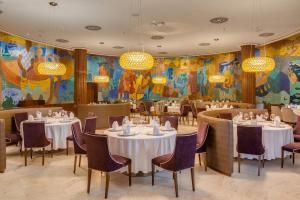 Sala de jantar elegante de restaurante com cadeiras roxas, toalhas de mesa brancas e paredes com murais coloridos.