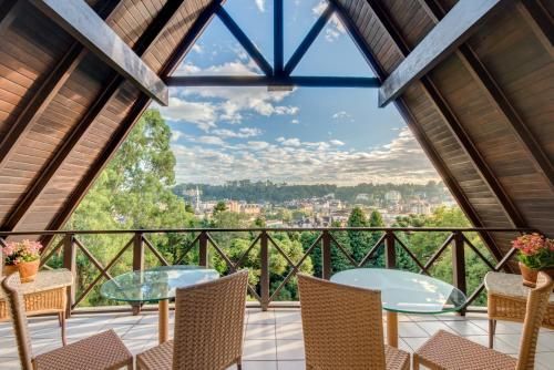 Terraço coberto com palha, com vista para um vale tropical e para a cidade, com cadeiras de vime e mesa de vidro sob um teto aberto.