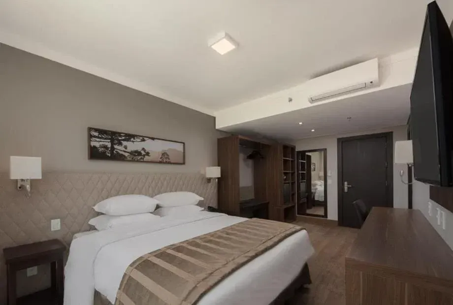 Quarto de hotel moderno com cama arrumada, obras de arte na parede, TV, escrivaninha e ar-condicionado.