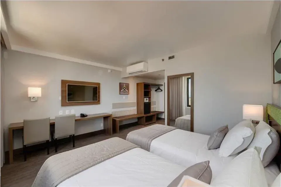 Quarto de hotel moderno com duas camas, escrivaninha, espelho de parede e iluminação suave.