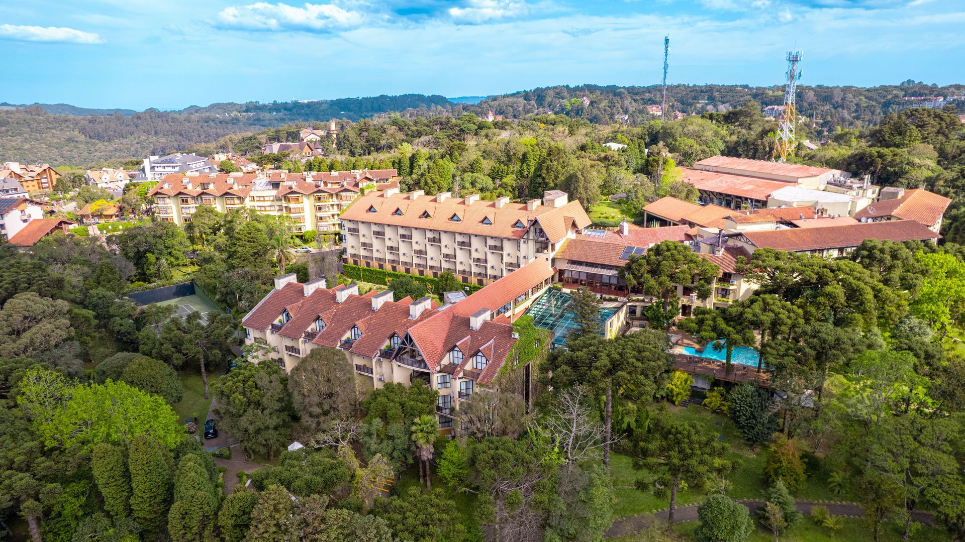 Vista aérea de edifícios com telhados vermelhos entre árvores em uma cidade na encosta de uma colina, com o horizonte ao longe.