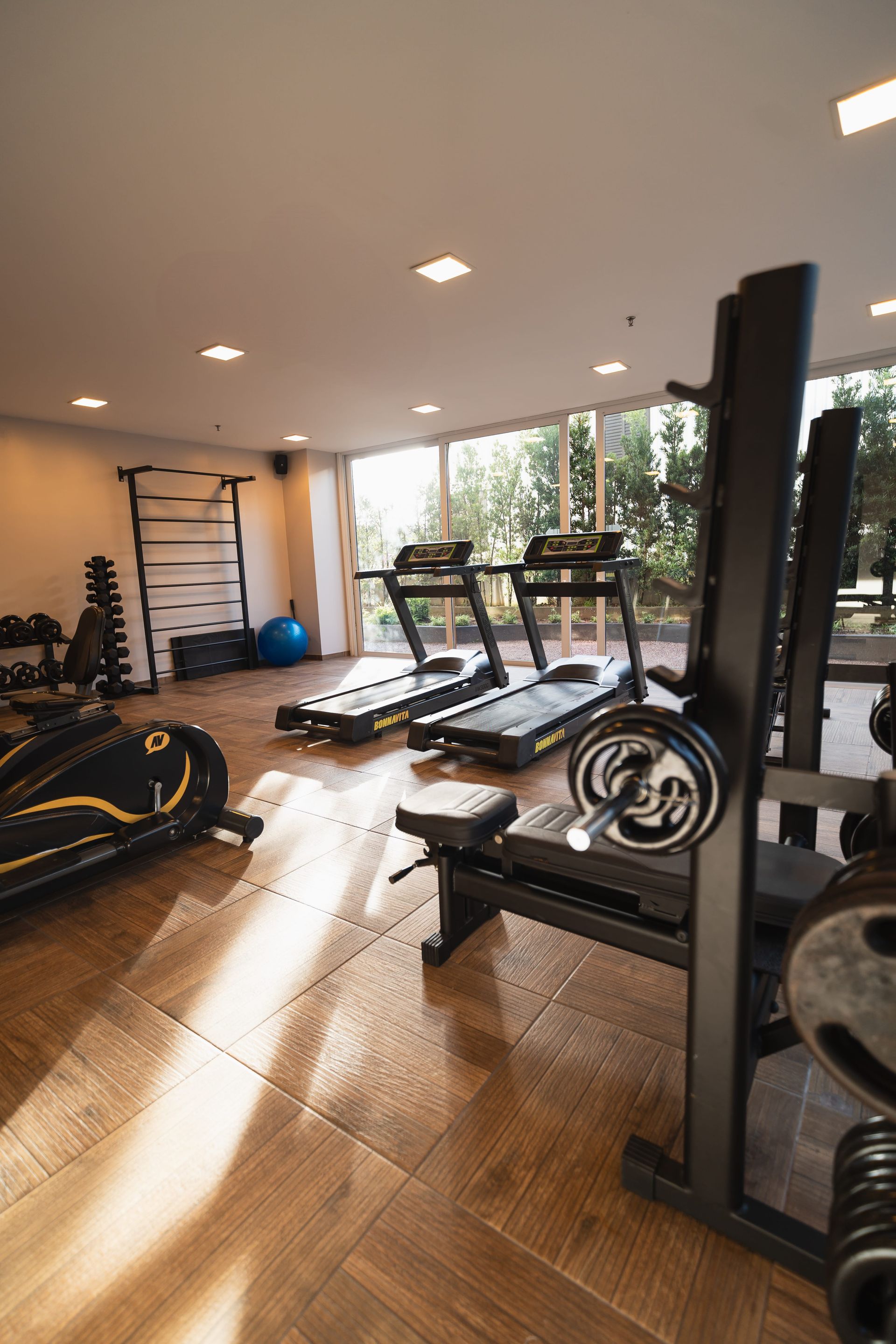 Academia moderna com esteiras, aparelhos de musculação e halteres em um piso de madeira polida.