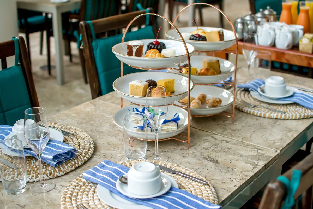 Prepare uma mesa de chá com uma bandeja de vários andares, porcelana azul e branca e jogos americanos de vime sobre uma mesa rústica de madeira.