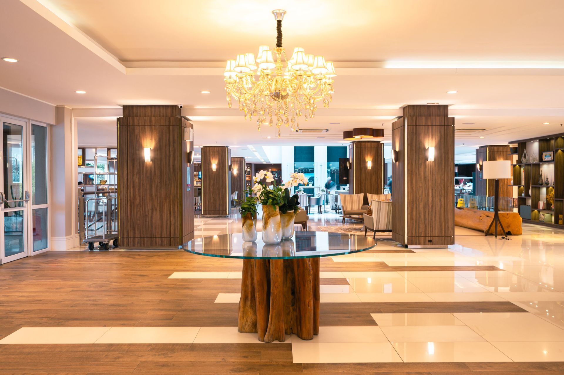 Hall de entrada elegante do hotel com lustre, colunas de madeira e um arranjo floral central sobre uma mesa redonda.