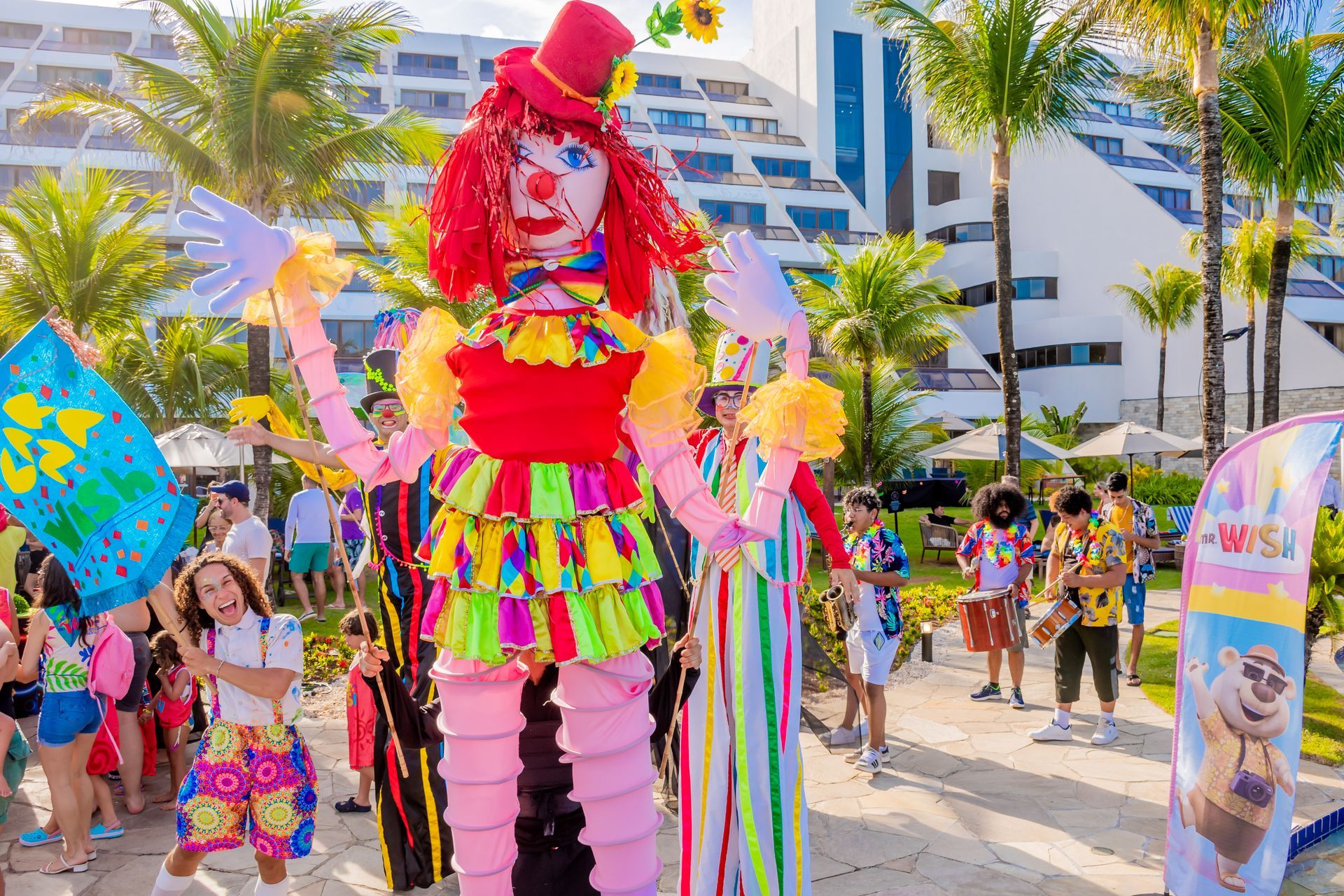 Quatro crianças com fantasias listradas segurando bolos decorados em um cenário de festa colorido.