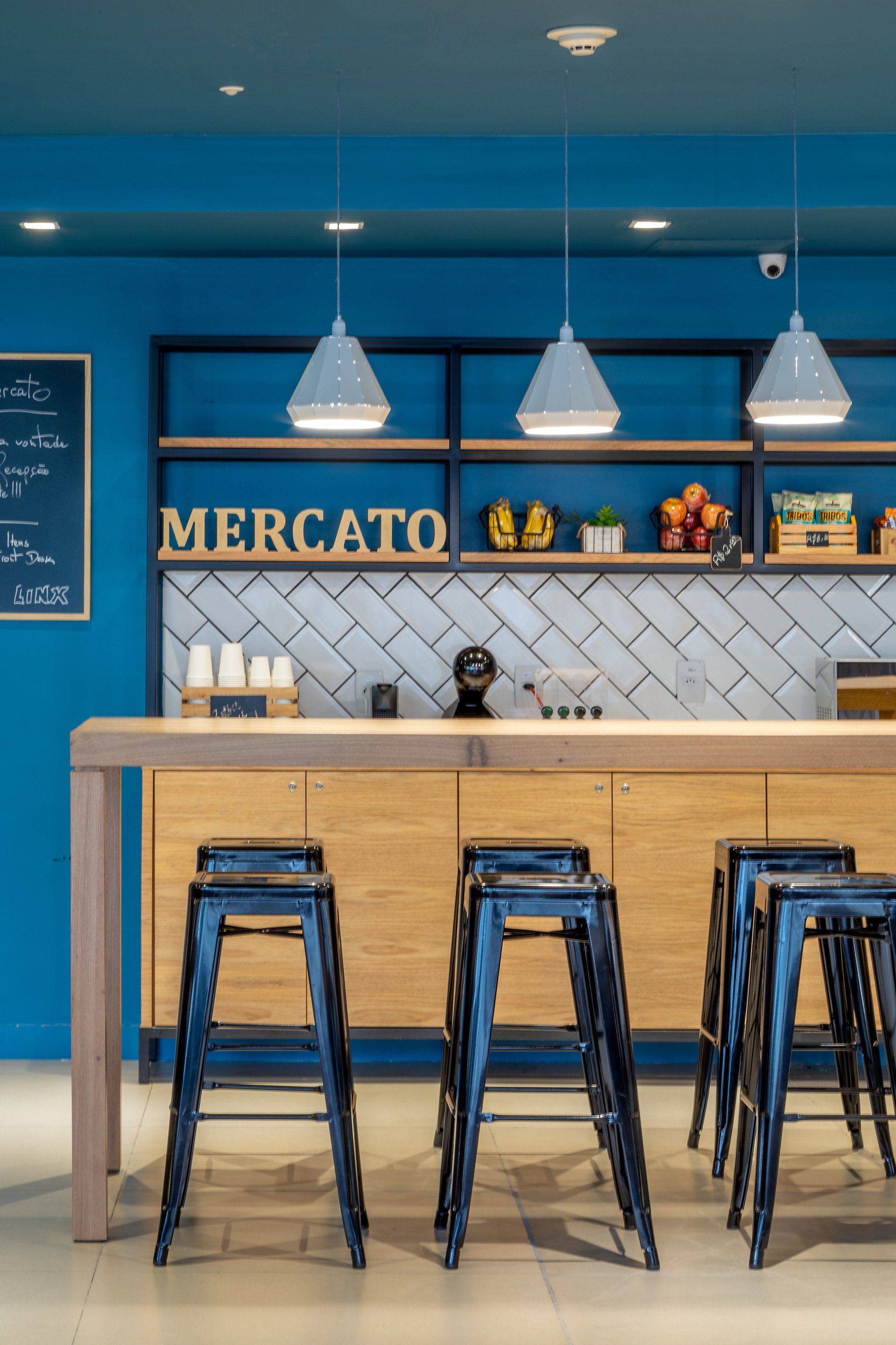 Interior de café azul com balcão de madeira, luminárias pendentes e banquetas altas pretas.